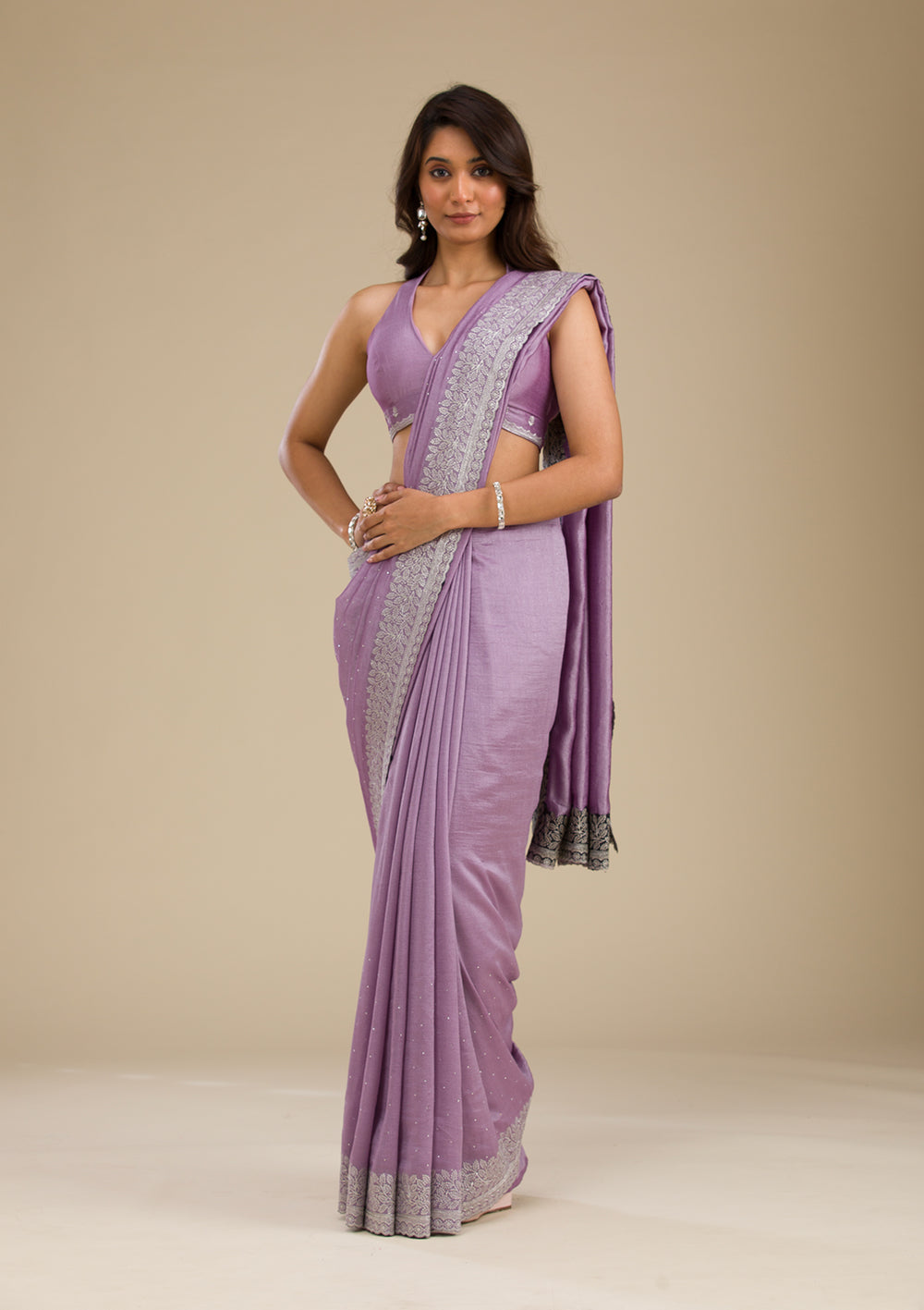 A woman modeling a purple saree with silver zariwork, showcasing the fabric and design.